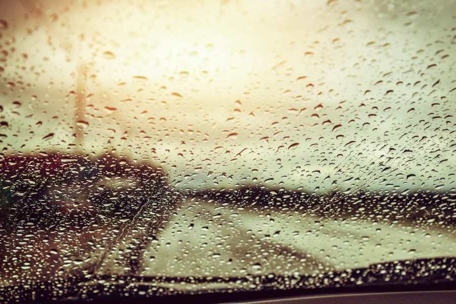 Raindrops cover the windshield of a car racing down the highway.