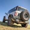 White Ford Bronco covered in mud and parked in a field off-road.