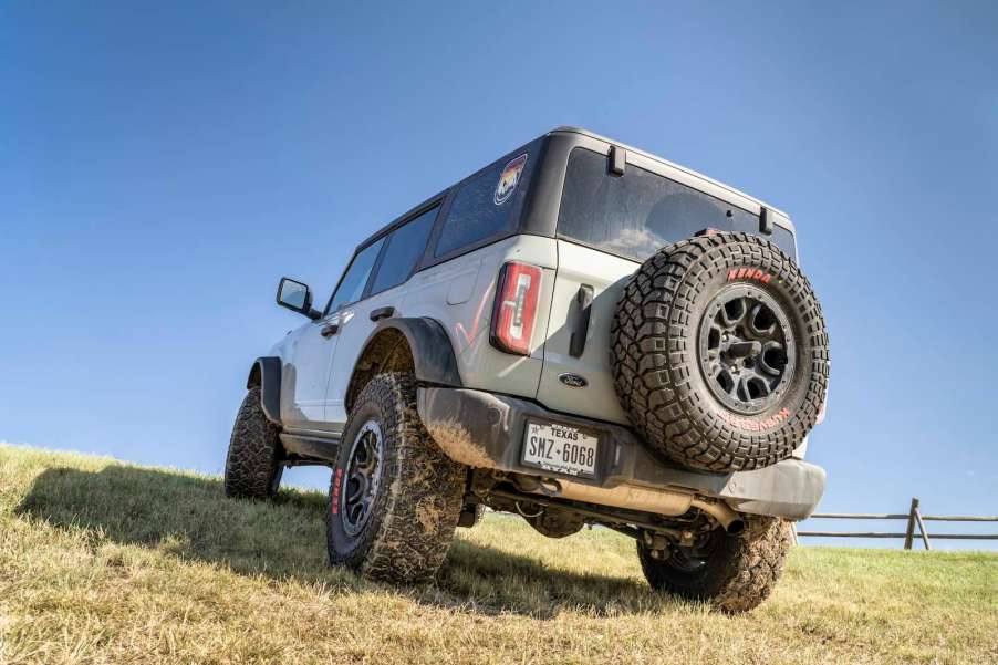 White Ford Bronco covered in mud and parked in a field off-road.