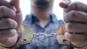 A car thief in handcuffs after police officers pulled him out of a stolen car.