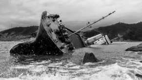 Black and white photo of a rapidly sinking ship, the coastline visible in the background.