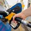 A hand putting a fuel filler nozzle into a blue car at at a gas station