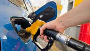 A hand putting a fuel filler nozzle into a blue car at at a gas station