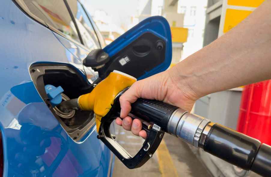 A hand putting a fuel filler nozzle into a blue car at at a gas station