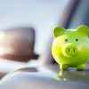 A green piggy bank sits atop a silver car's hood in close right front view