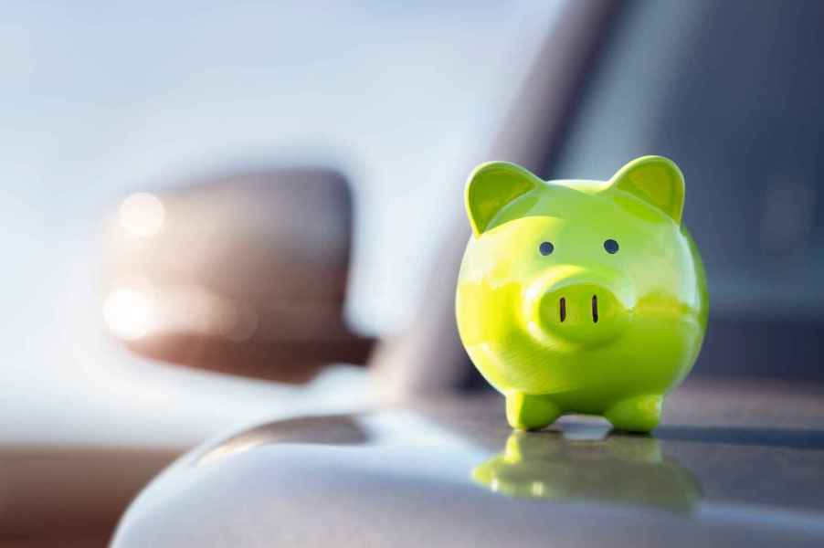 A green piggy bank sits atop a silver car's hood in close right front view