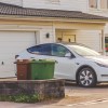 A white Tesla EV parked outside a home garage on the driveway