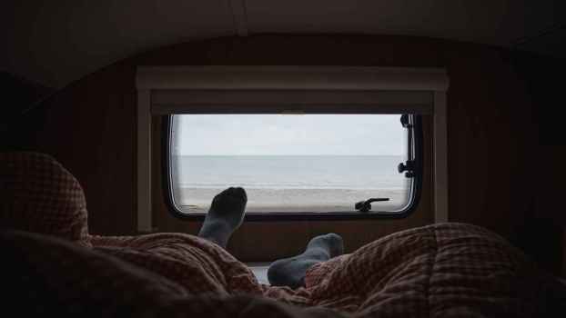 A sleeping van lifer's legs and socks shown near a camper window looking outdoors