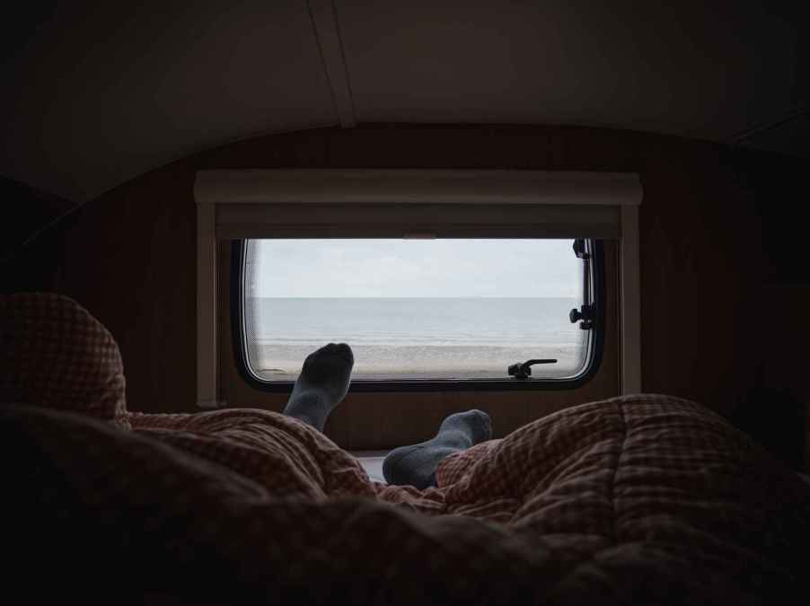 A sleeping van lifer's legs and socks shown near a camper window looking outdoors